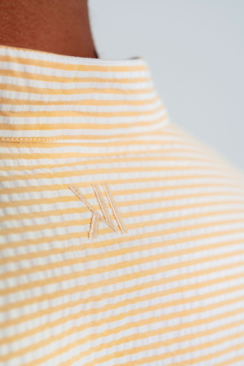 Close-up of DUSKITTEN tone-on-tone logo embroidery under the back collar of the SOLAR DRIFT shirt, showing cream and yellow stripe seersucker texture detail, Duskened Genesis collection.