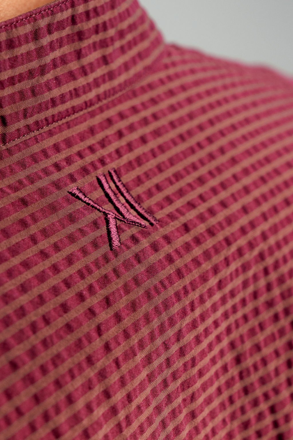 Close-up of DUSKITTEN tone-on-tone logo embroidery under the back collar of the OXBLOOD MERIDIAN shirt, showing seersucker texture detail, Duskened Genesis collection.